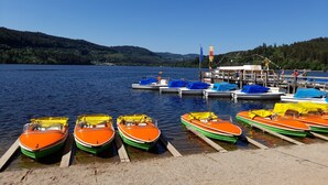 A lakeside dock with several colorful boats, a wooden pier, and a building with a flag. - Apartment 'Kopffrei on 1000 m² /Apartment 2 with Shared Garden, Balcony & Wi-Fi (Feldberg (Schwarzwald))