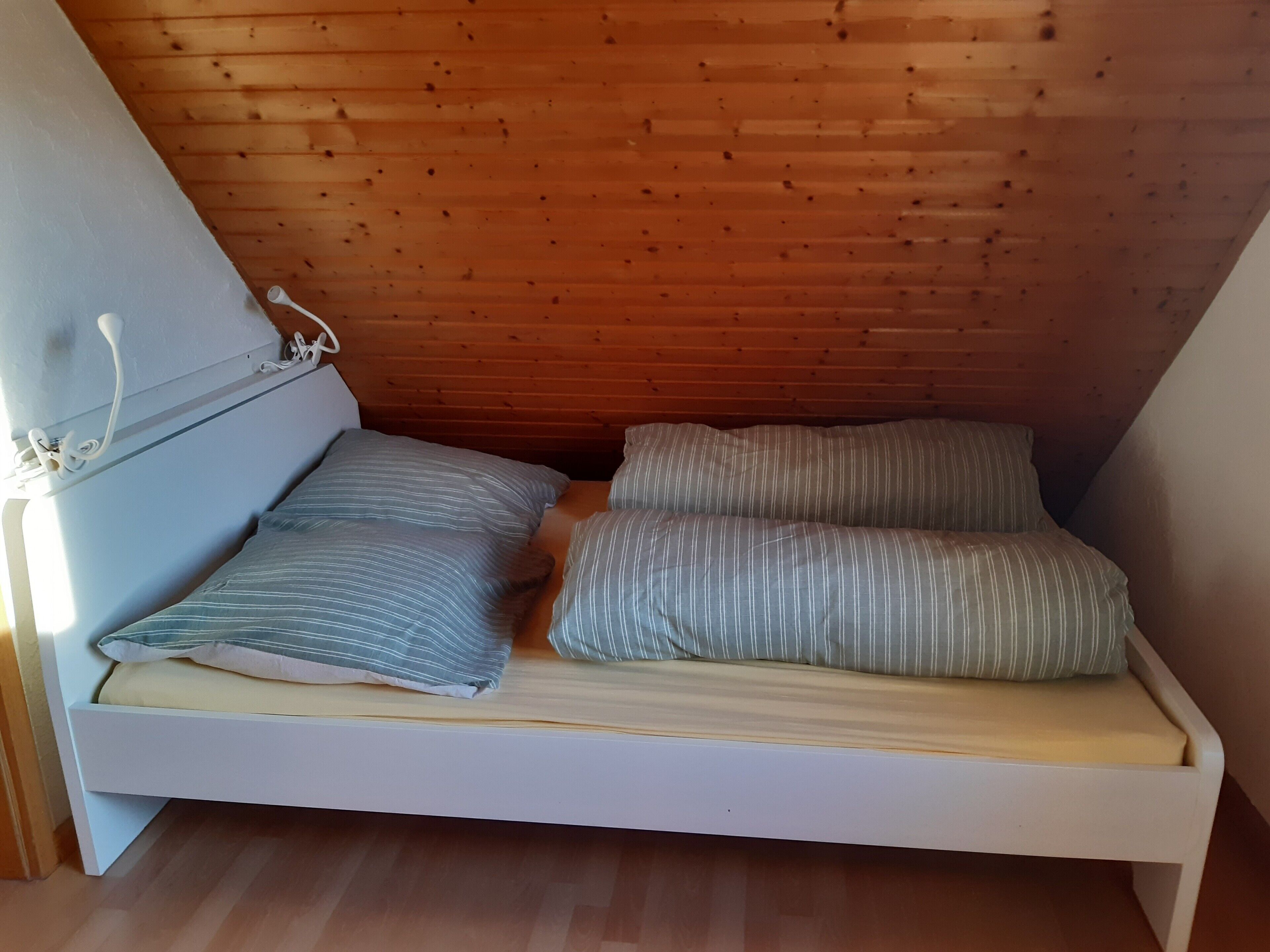 A small, single-bed room with wooden slats on the ceiling and a white bed frame.