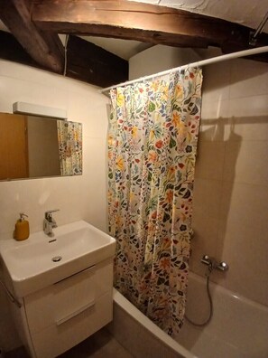 Ein Badezimmer mit weißem Waschbecken, Spiegel und einer Duschvorhang mit Blumenmuster.