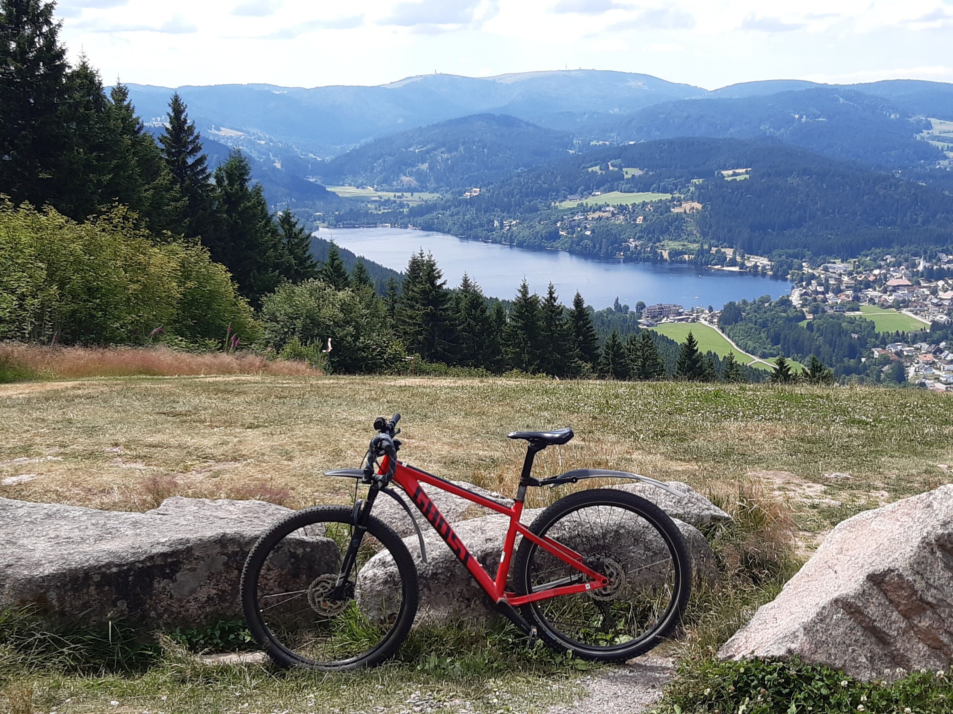 A mountain bike parked on a grassy hill with a lake and town in the background.