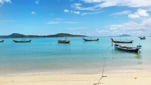 A beach with several boats anchored in calm waters, a sandy shore, and distant hills. - Beachside 1BR•Walk to Rawai•Cozy-title rawai C201 (ตำบล ราไวย์)