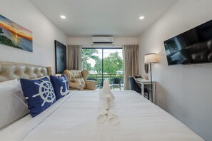 Habitación de hotel con una cama, televisor, sillón y vistas a zonas verdes.