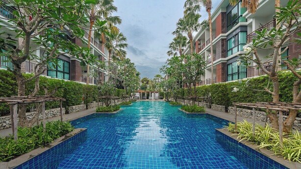 A swimming pool with a tiled floor, surrounded by greenery and buildings with balconies. - Beachside 1BR•Walk to Rawai•Cozy-title rawai C201 (ตำบล ราไวย์)