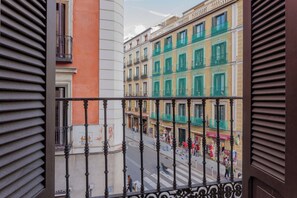 Ein Balkon mit Blick auf eine Straße, an der sich Gebäude, eine Fußgängerampel und Fußgänger befinden.
