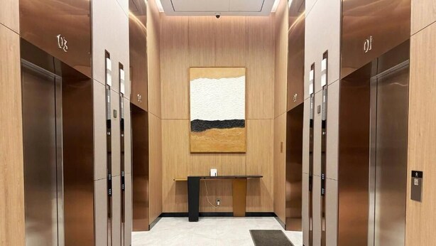 A modern elevator lobby with a central reception desk, two elevators, and a large abstract painting on the wall. - Apartment in Icon 40 Ha Long   (Bai Chay)