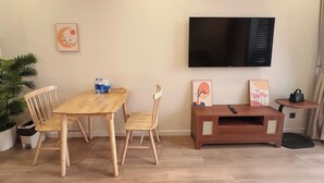 A living room with a wooden dining table, two chairs, a TV mounted on the wall, and a small wooden side table with a remote control. - Apartment in Icon 40 Ha Long   (Bai Chay)