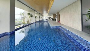 A long indoor swimming pool with tiled blue floor and walls, wooden ceiling, and large windows offering a view of the city. - Apartment in Icon 40 Ha Long   (Bai Chay)