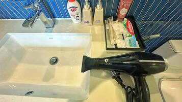 A bathroom sink with toiletries, a hairdryer, and a bottle of shampoo.
