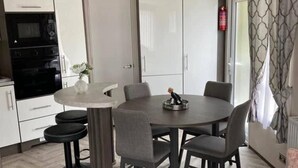 Una cocina moderna con armarios blancos, un horno negro y un comedor con una mesa redonda y seis sillas.