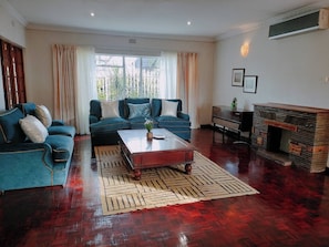 A living room with a sofa set, a coffee table, a fireplace, and a view through the window. - Spacious Home, Families & Crews, Near Northcliff (Johannesburg)