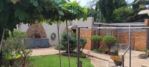 A brick patio with a grill, a pergola, and a small garden area with potted plants and a lawn. - Spacious Home, Families & Crews, Near Northcliff (Johannesburg)