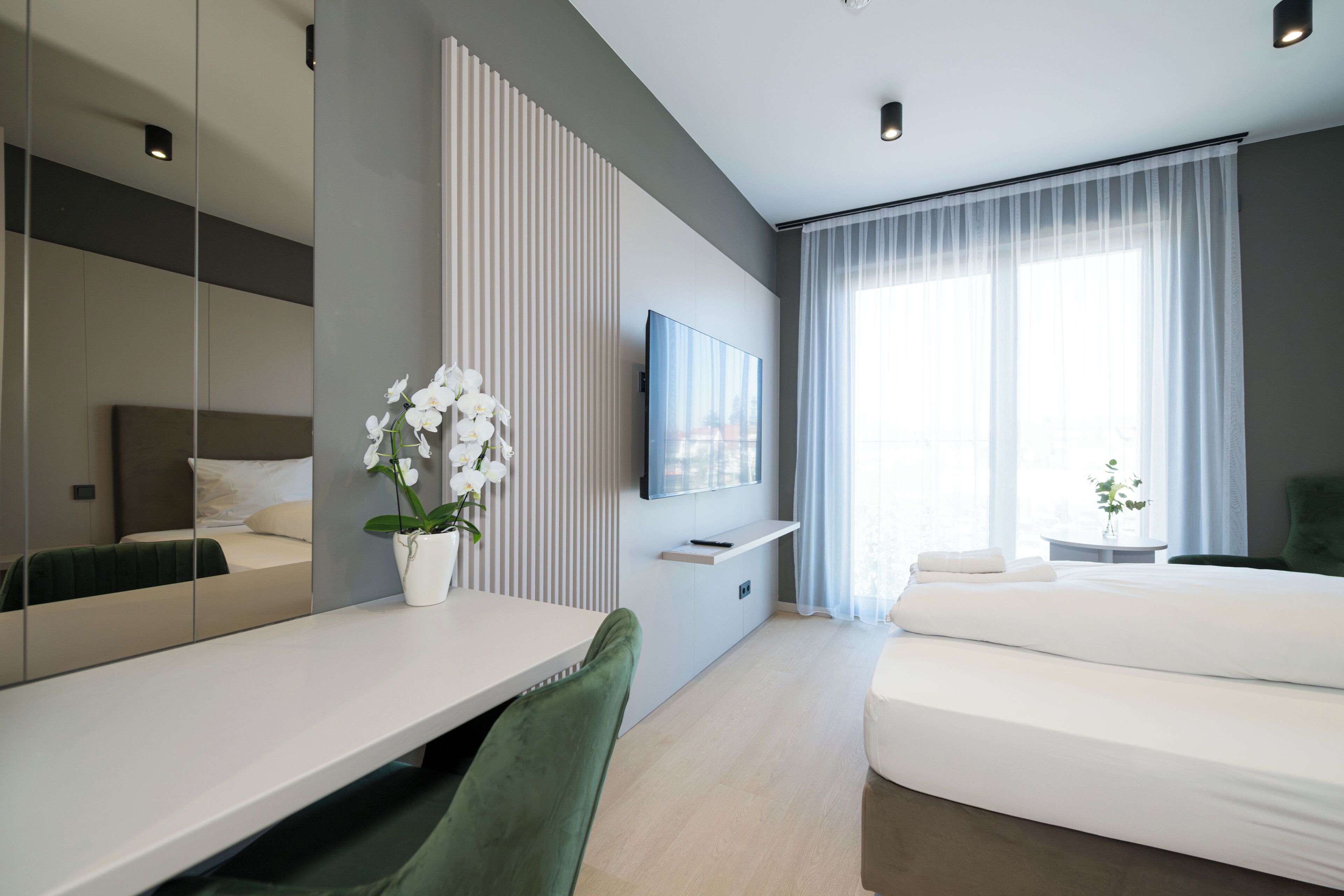 A modern hotel room with a bed, a desk, a chair, a TV, and a window with curtains.