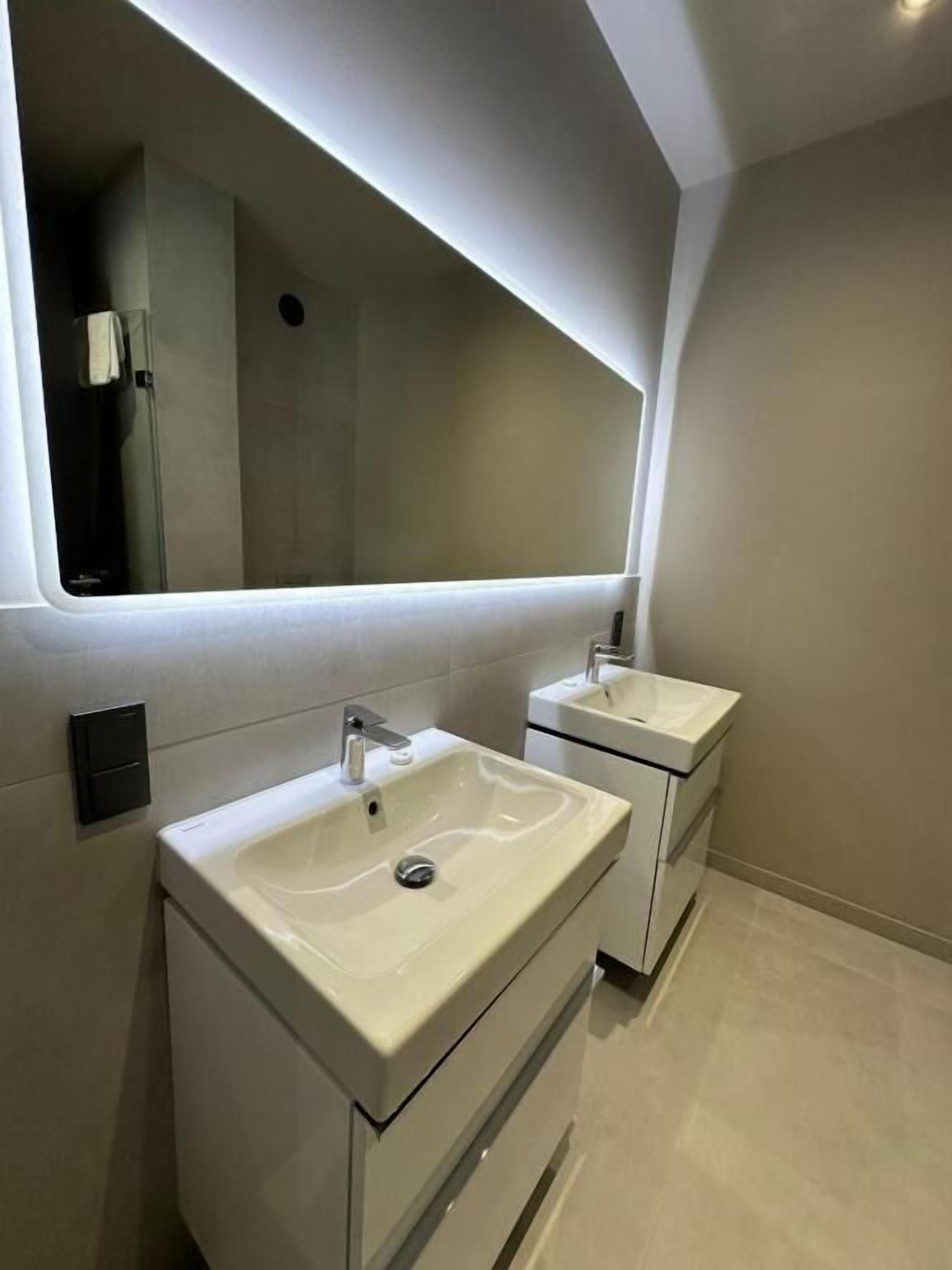 Een moderne badkamer met twee wastafels, een grote spiegel en een inbouw plafondlamp.