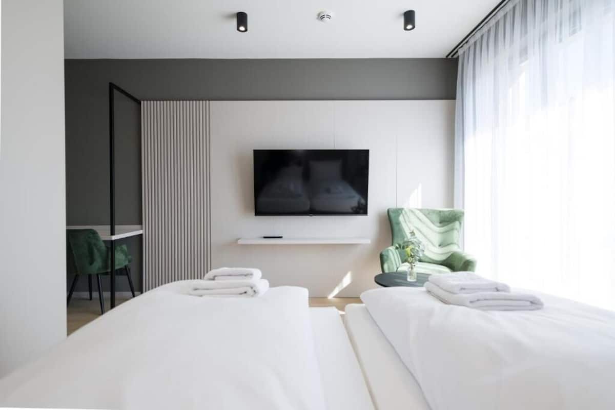 A modern hotel room with a bed, a TV, a desk, and a chair.