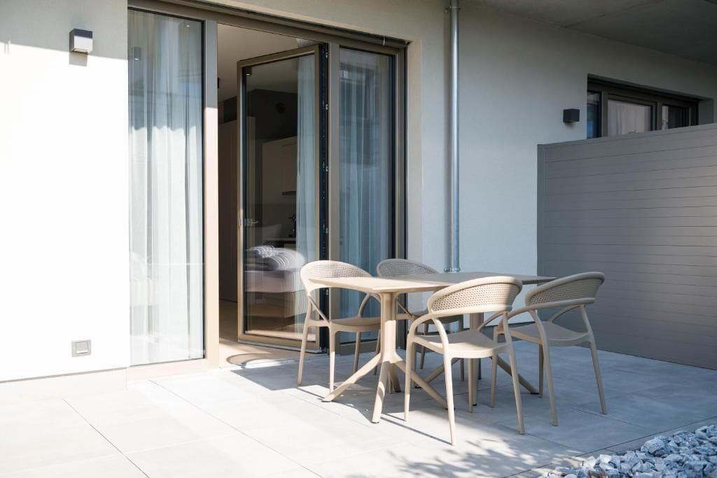 Une terrasse extérieure moderne avec une table et des chaises, une porte-fenêtre coulissante donnant sur une pièce et un mur gris.