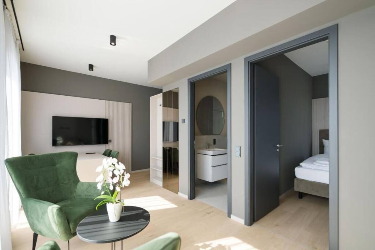 A modern hotel room with a flat-screen TV, a green armchair, a small round table, and a potted orchid.
