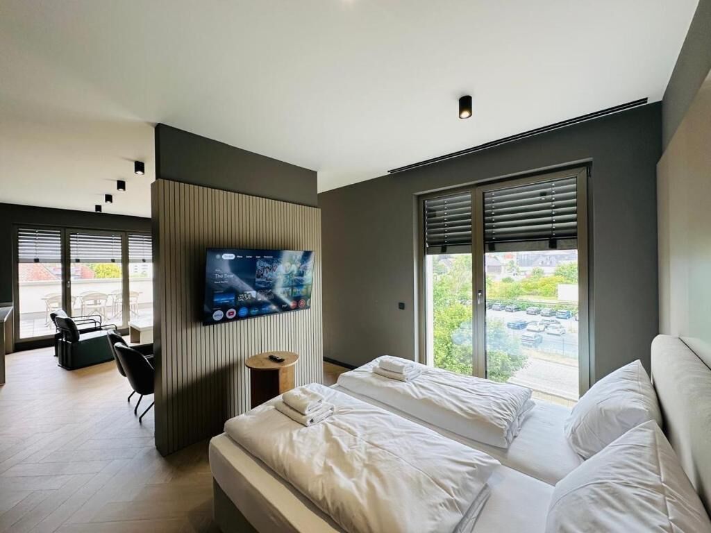 Een moderne hotelkamer met een bed, een televisie, een raam met jaloezieën en uitzicht op buiten.