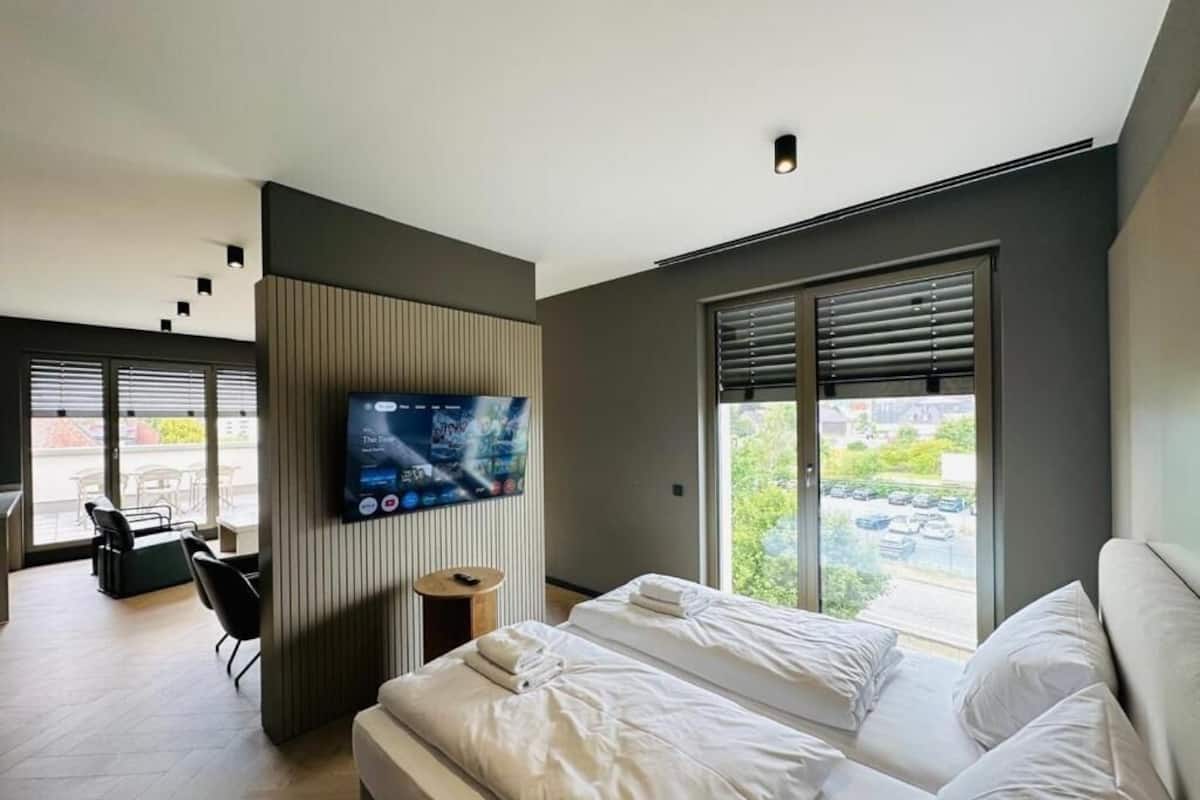 Ett modernt hotellrum med en säng, en TV, ett fönster med persienner och utsikt över omgivningarna.