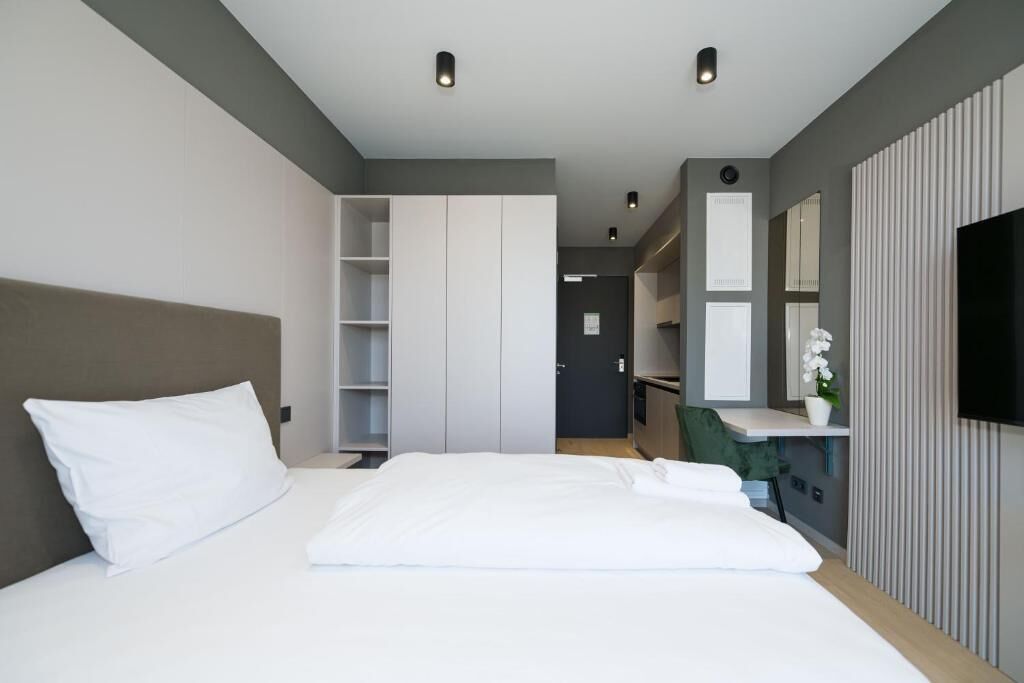 Una camera d'albergo moderna con un ampio letto, armadio a muro, una scrivania con sedia e televisione montata a parete.