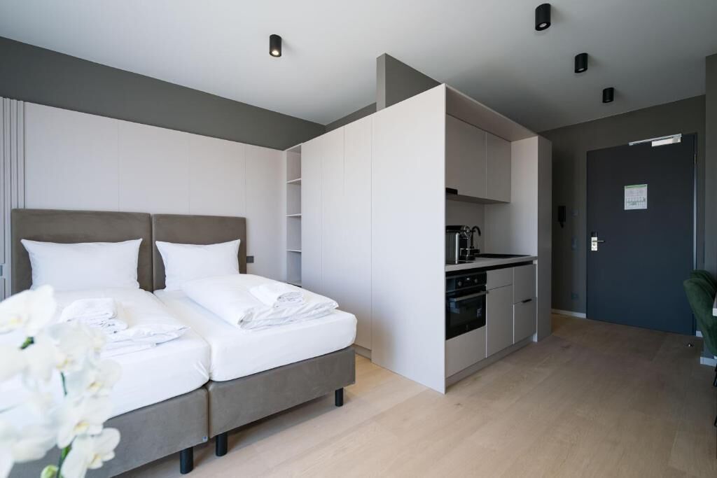 Une chambre d’hôtel moderne équipée d’un lit, d’une kitchenette et d’une porte donnant sur une autre pièce.