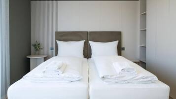 A double bed with white linens and towels, a bedside table with a vase, and a vertical panel on the wall.