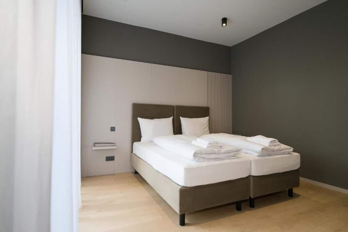 A modern bedroom with a double bed, a bedside table, and a large window.