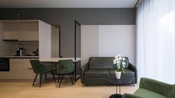 A modern living space with a sofa, a dining table, two chairs, and a potted plant.