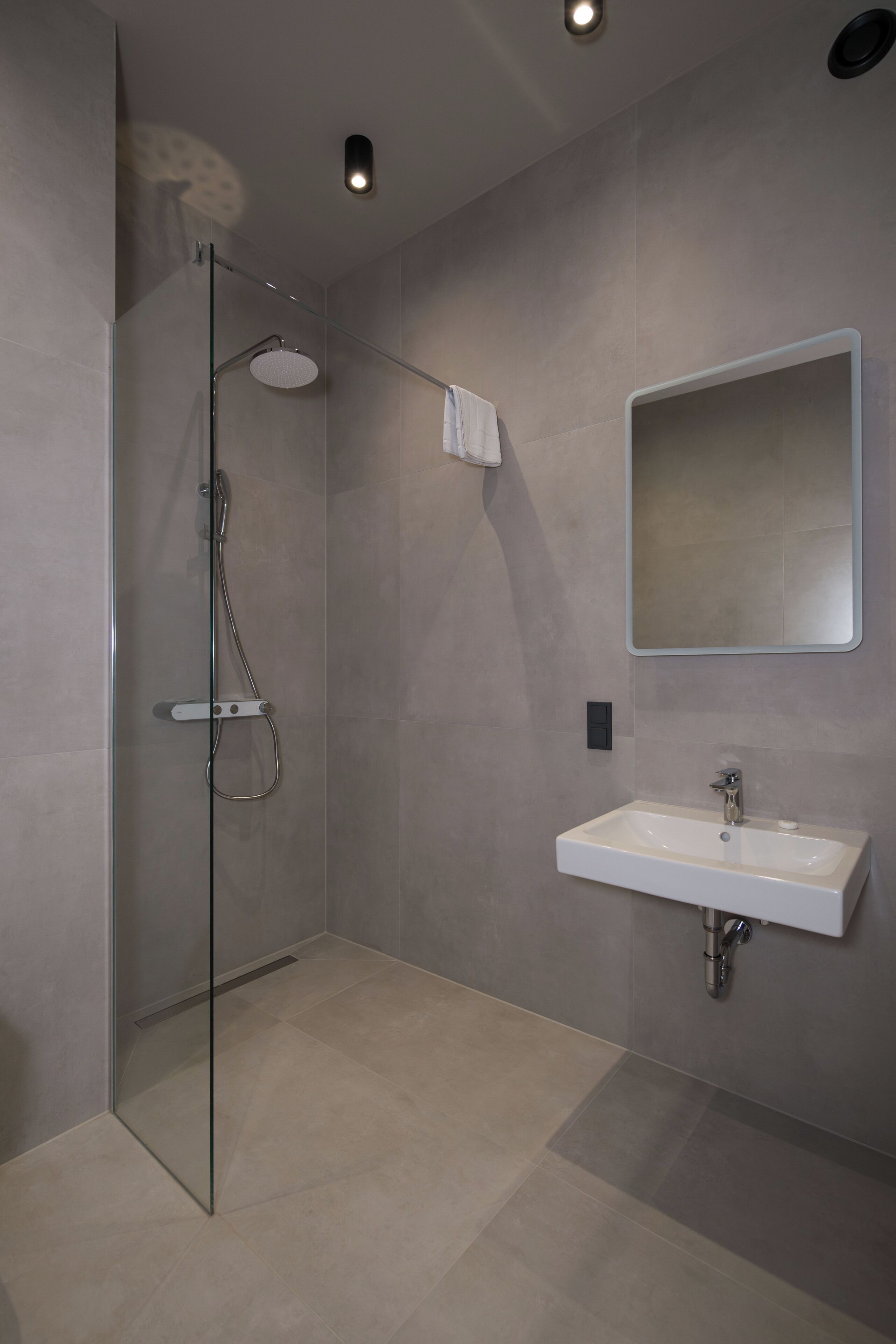 Un baño moderno con cabina de ducha de vidrio, un lavamanos blanco y un espejo grande.