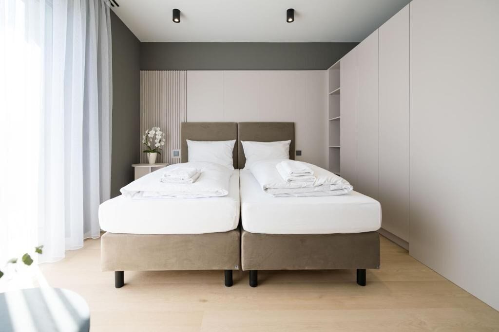 Ein modernes Schlafzimmer mit zwei Betten, einem Nachttisch mit Lampe und einem Fenster mit Vorhängen.