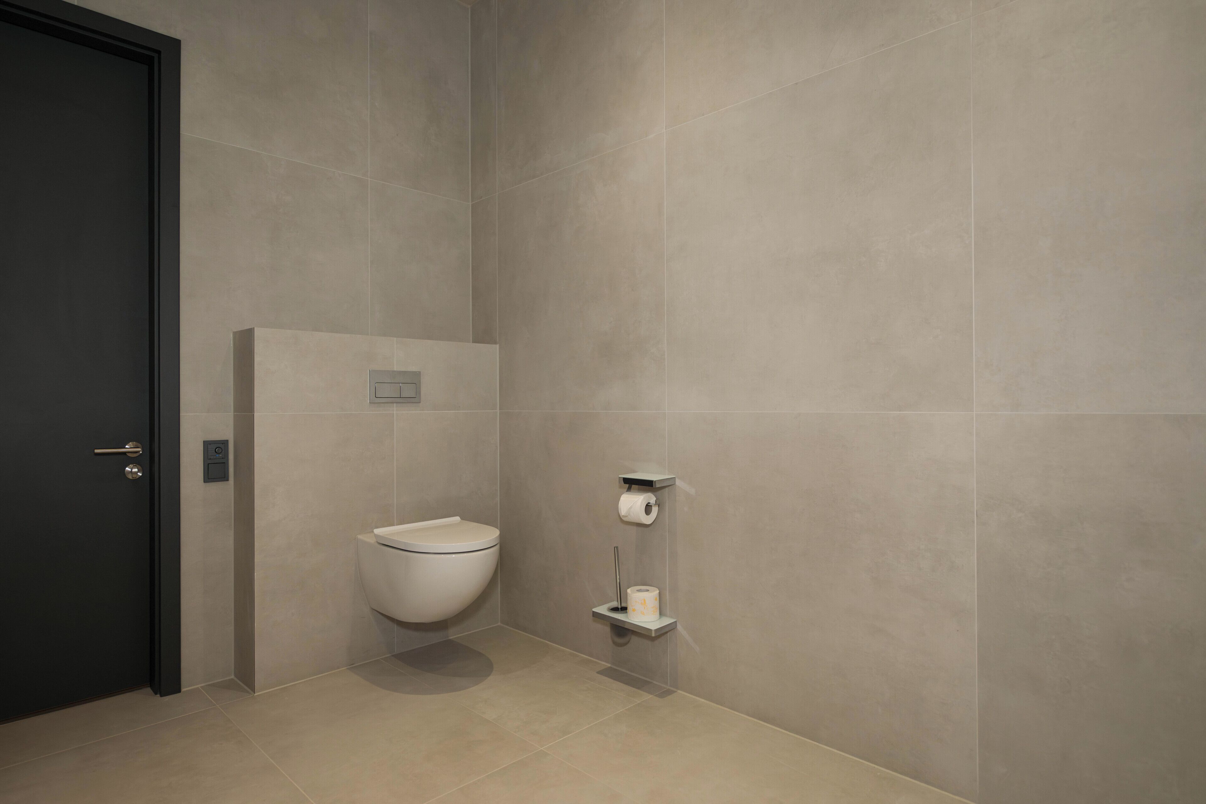 Ein modernes Badezimmer mit Toilette, Ablage für Toilettenpapier und einer Tür.