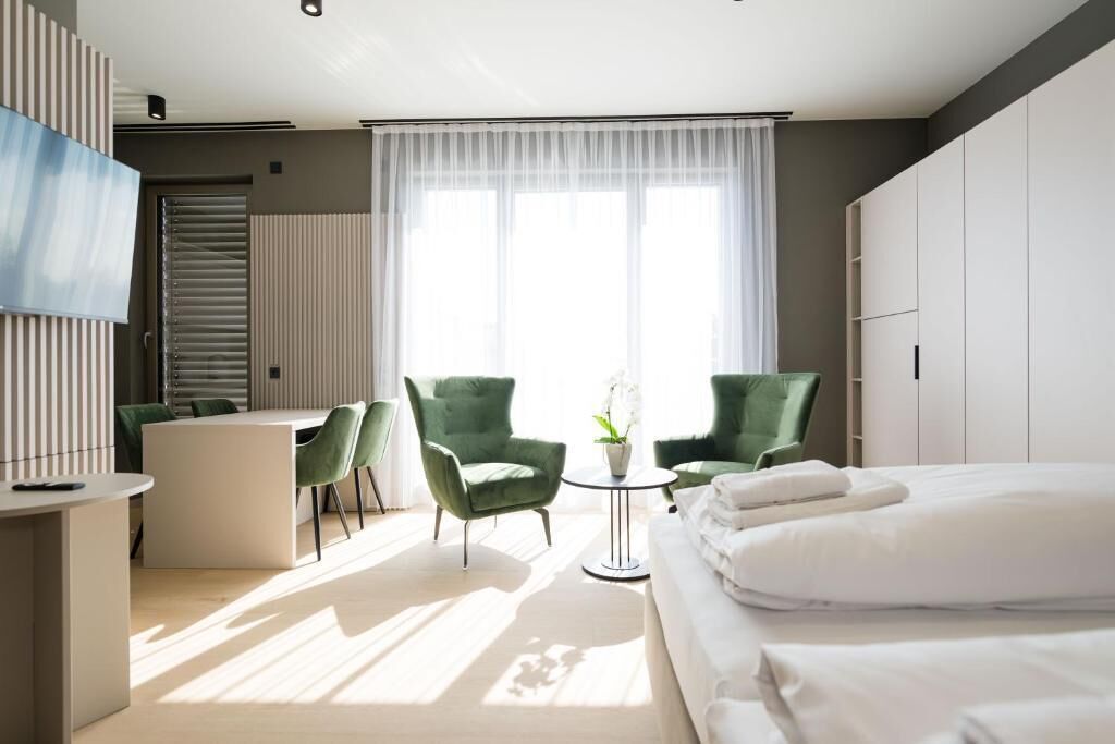 Camera d'albergo moderna con un letto, una scrivania, due sedie, un tavolino con una pianta e una TV appesa al muro.