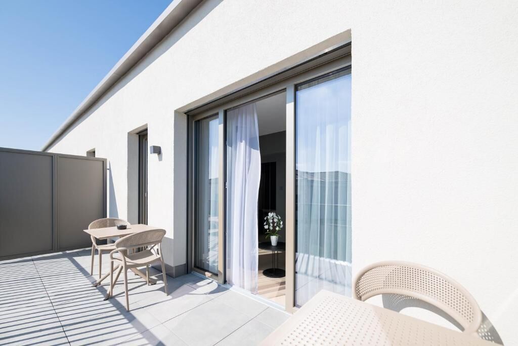 Ein moderner Balkon mit Tisch, Stühlen, einer Schiebeglastür und einem Blumentopf.