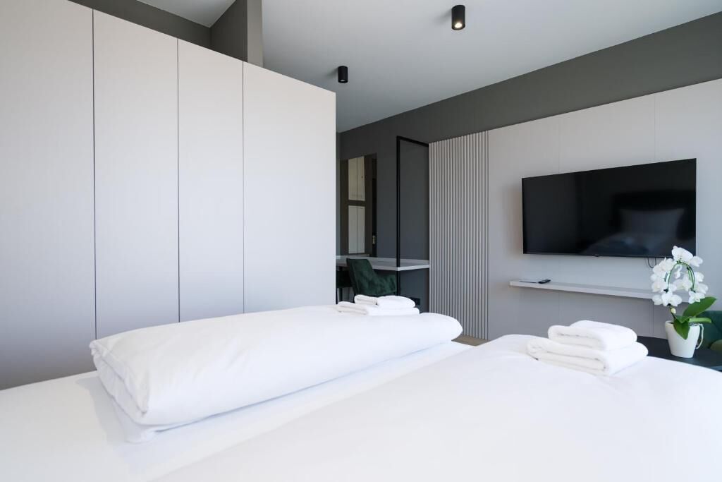 A modern hotel room with a bed, a flat-screen TV mounted on the wall, a small desk, and a potted orchid.