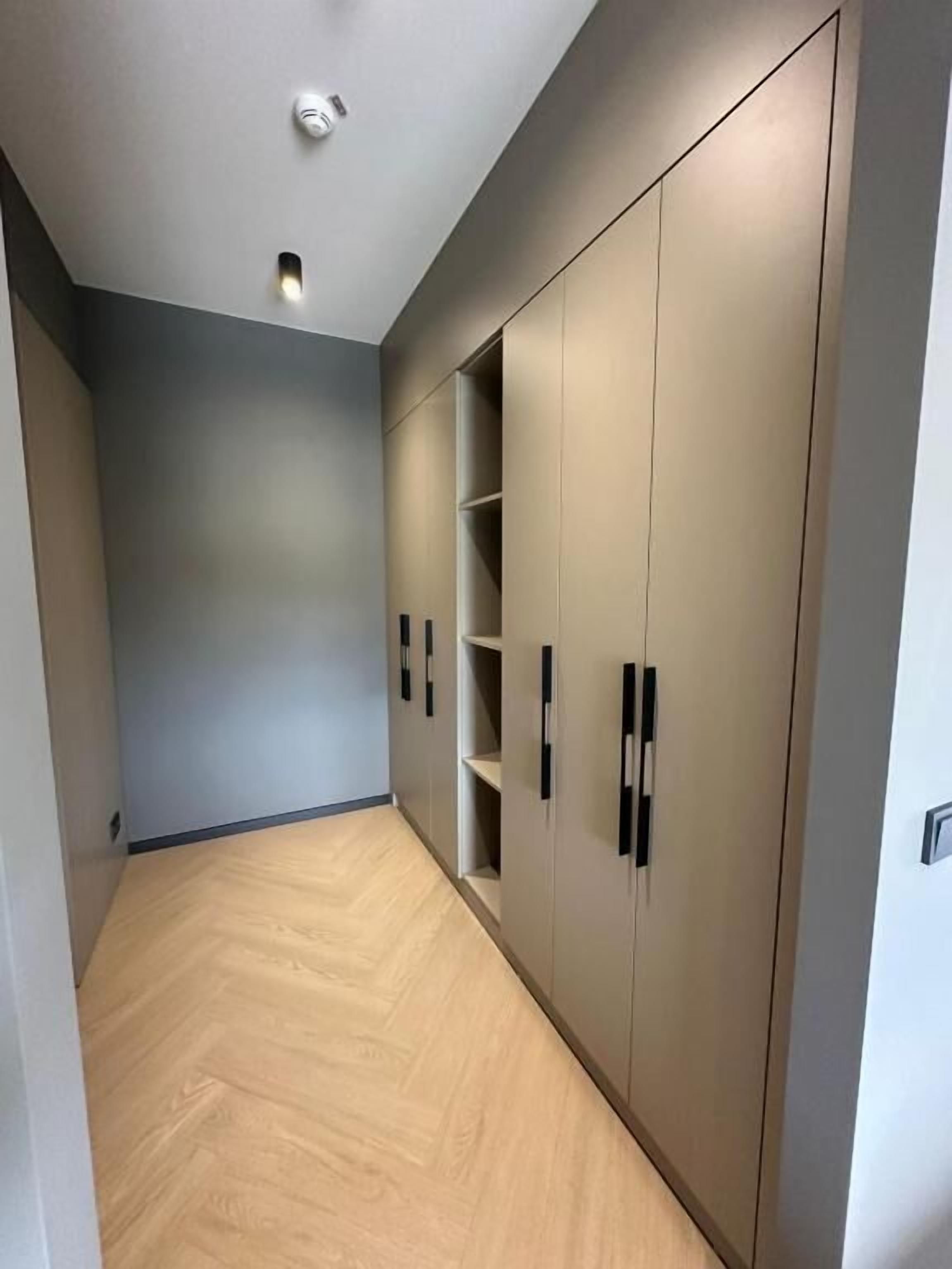 Un pasillo con suelo de madera, pared gris y un armario grande con múltiples puertas y estantes.