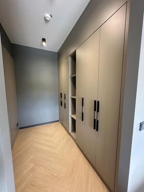Um corredor com piso de madeira, parede cinza e um guarda-roupa grande com várias portas e prateleiras.