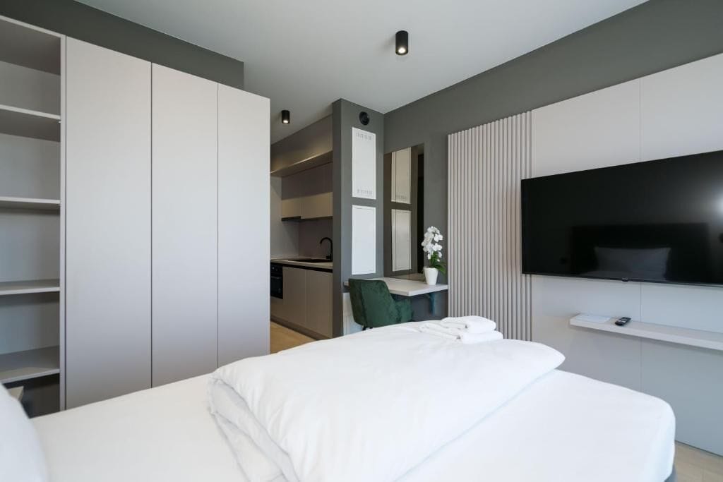 A modern hotel room with a bed, a TV, a desk, and a walk-in closet.