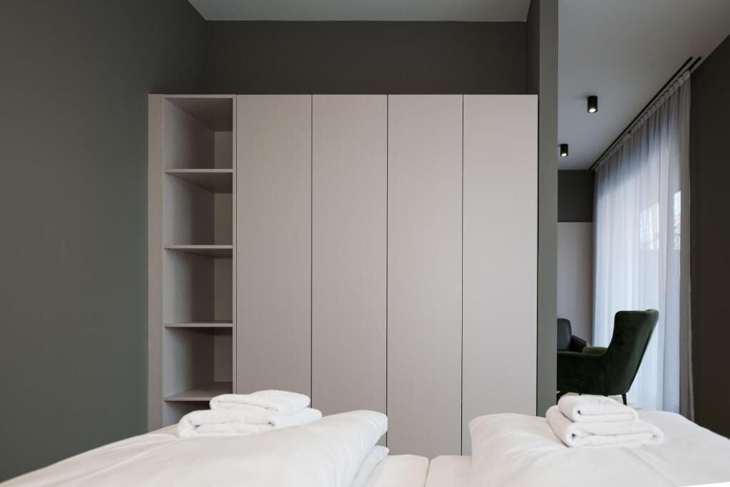 A modern hotel room with a large wardrobe, a bed with neatly folded white towels, and a chair by the window.