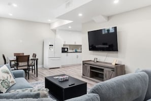 Un salon moderne avec un téléviseur à écran plat, un canapé, une table basse et un coin cuisine à l’arrière-plan.