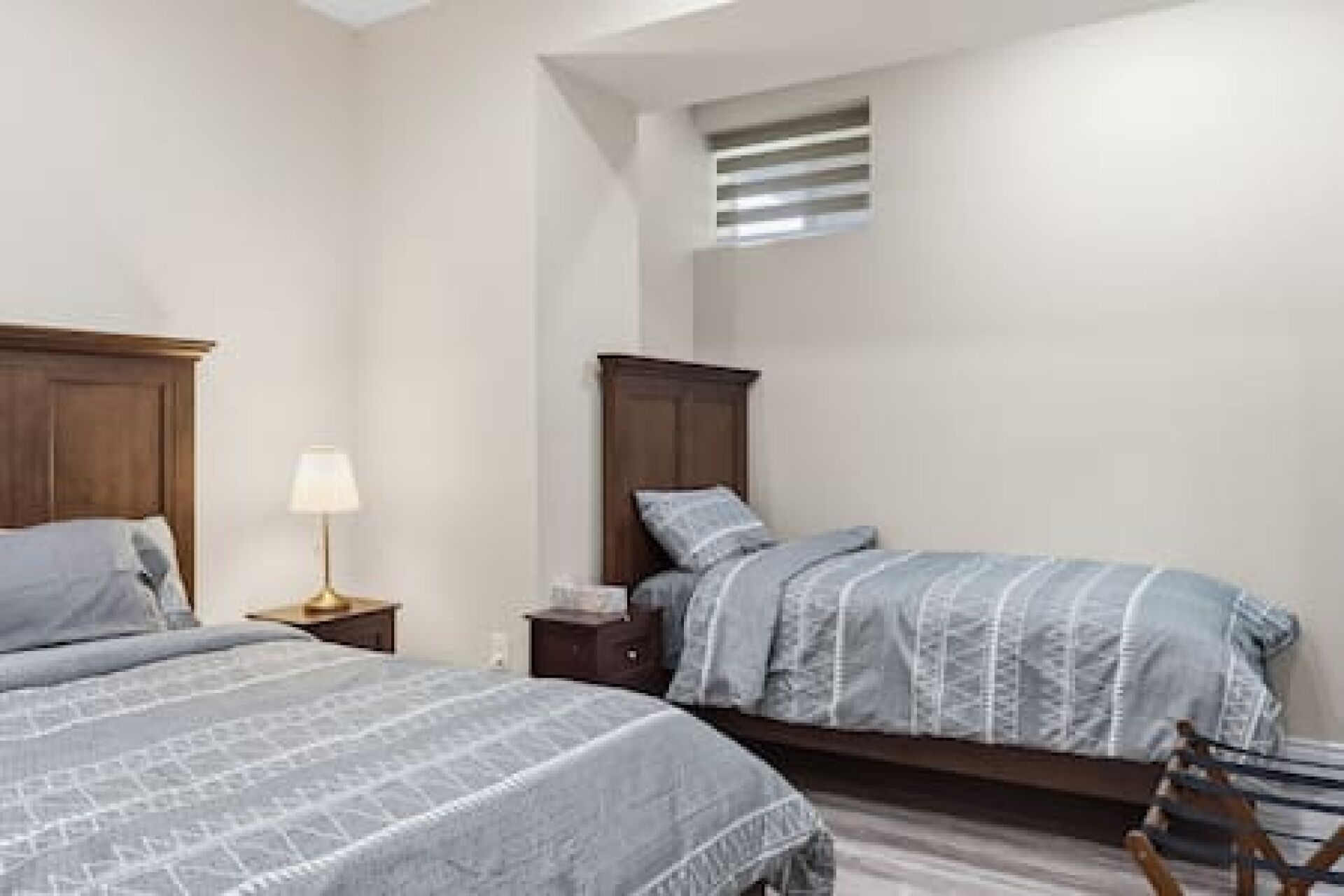 Een slaapkamer met twee bedden, een nachtkastje met een lamp en een klein raam.