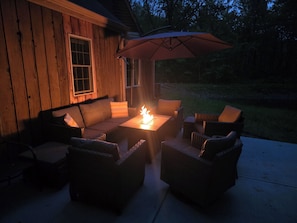Un patio al aire libre con una mesa de fuego, mobiliario de mimbre y una sombrilla.
