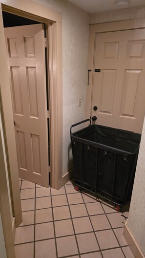 A hallway with a tiled floor, a partially open door, and a black storage bin against the wall.
