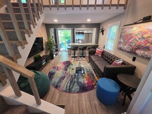 A modern living room with a staircase, a sofa, a coffee table, and a colorful rug.