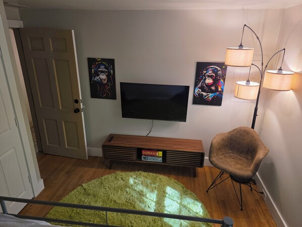 A living room with a flat-screen TV, a green furry rug, a brown chair, and two wall-mounted lamps.