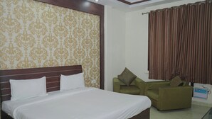 A hotel room with a large bed, a green armchair, and a curtain. - Infinity Hotel by Kalra Hotels Amritsar (Amritsar)
