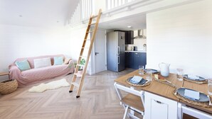 A loft-style living space with a wooden dining table set for four, a kitchen with modern appliances, a loft bed, and a ladder. - House - Sleeps 12 - Parking - Garden (Blandford Forum)