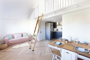 A loft-style living space with a wooden dining table set for four, a kitchen with modern appliances, a loft bed, and a ladder. - House - Sleeps 12 - Parking - Garden (Blandford Forum)