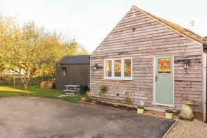A wooden cottage with a green door, a small porch, and a garden area with plants and a bird feeder. - House - Sleeps 12 - Parking - Garden (Blandford Forum)