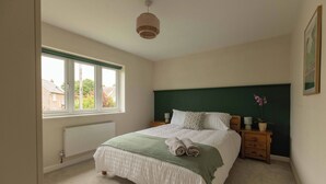 A bedroom with a bed, a window, a radiator, a nightstand, and a green headboard. - House - Sleeps 12 - Parking - Garden (Blandford Forum)