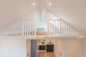 Une chambre à coucher aménagée dans un espace en hauteur, avec un lit superposé, une échelle en bois, un coin cuisine et une salle de bain.