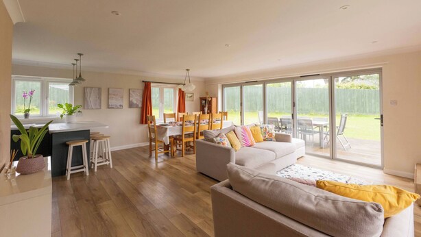 A spacious living area with a sofa, dining table, and chairs, large windows, and a kitchen area. - House - Sleeps 12 - Parking - Garden (Blandford Forum)